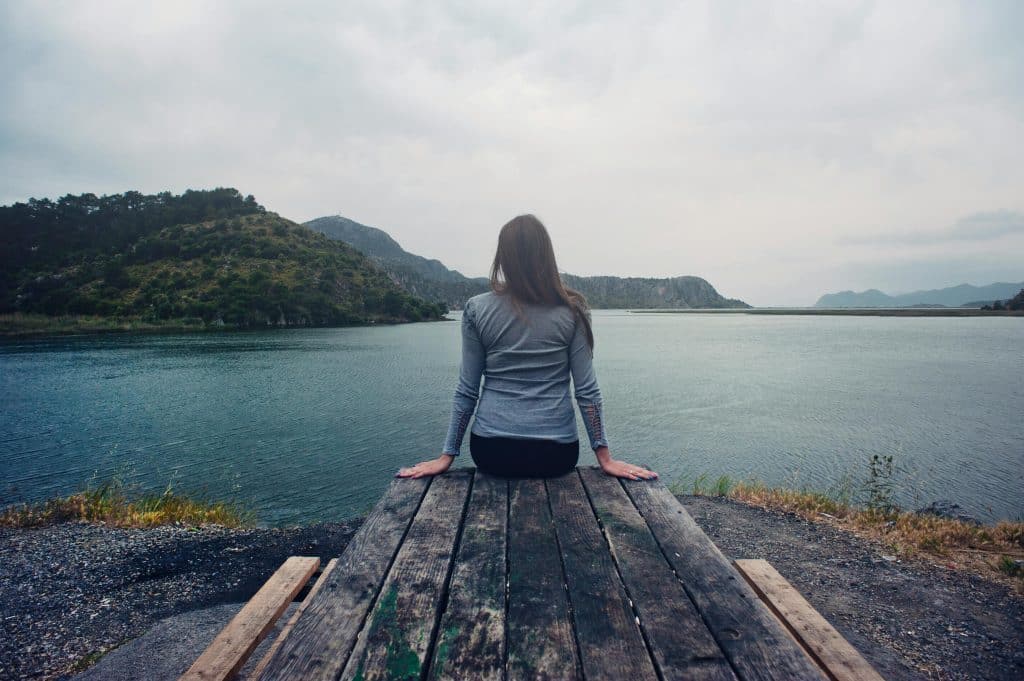 woman sitting on deck looking over lake